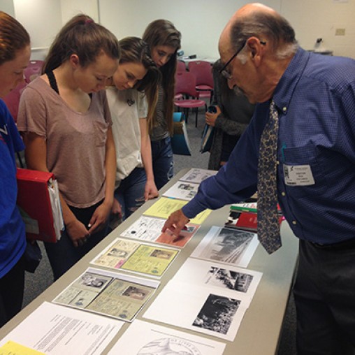 holocaust survivor speaking to a group of students around a table pointing