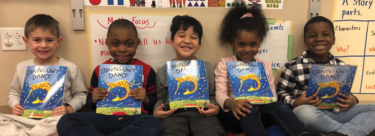 group of young students holding a book titled giraffes can't dance