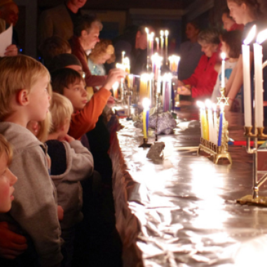 Group og adults and children lighting Hanukkah menorahs