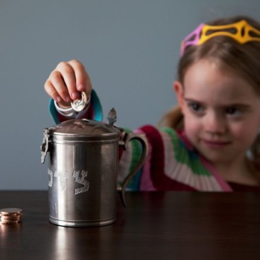 Little girl putting money into a tzedakah box