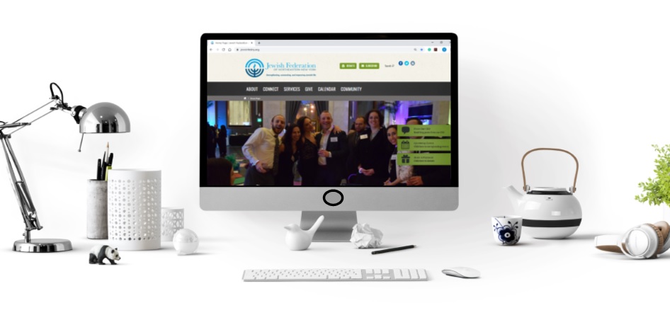 Desk with a computer screen showing Jewish Federation of Northeastern New York's homepage of website